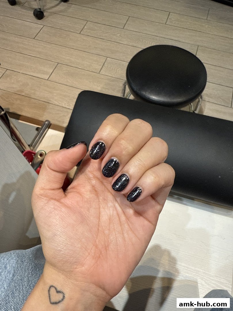 A hand with freshly painted black glitter nails and a heart tattoo on the wrist.