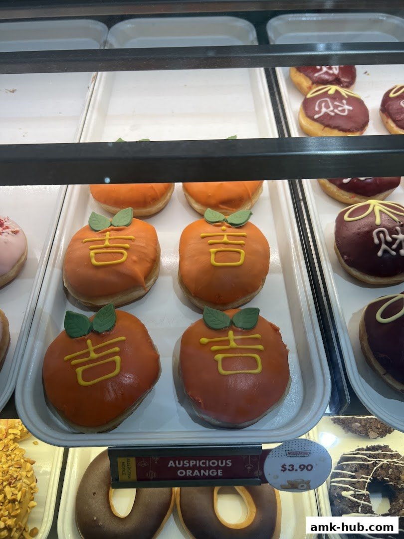 A display case filled with assorted Krispy Kreme donuts, featuring orange-frosted donuts with Chinese characters.