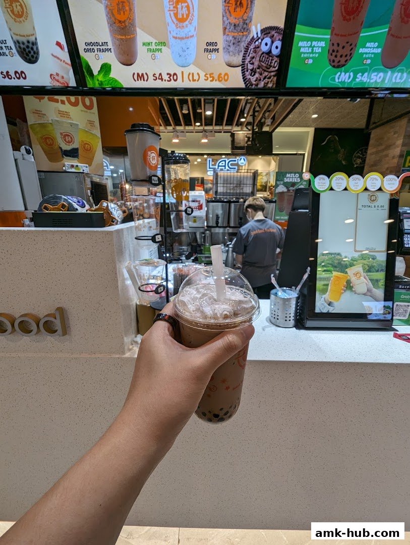 A hand holds a bubble tea drink in front of the Each A Cup counter.
