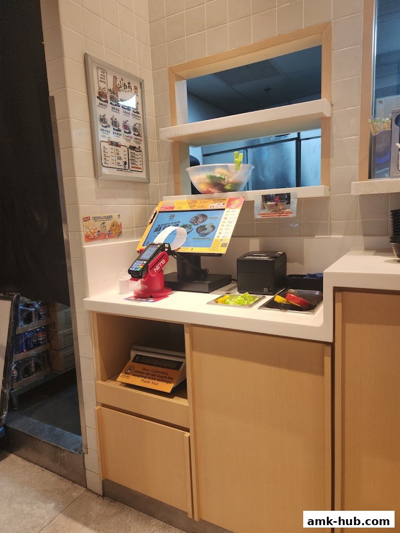 A counter with a digital menu, payment terminal, and ingredients for mala tang.