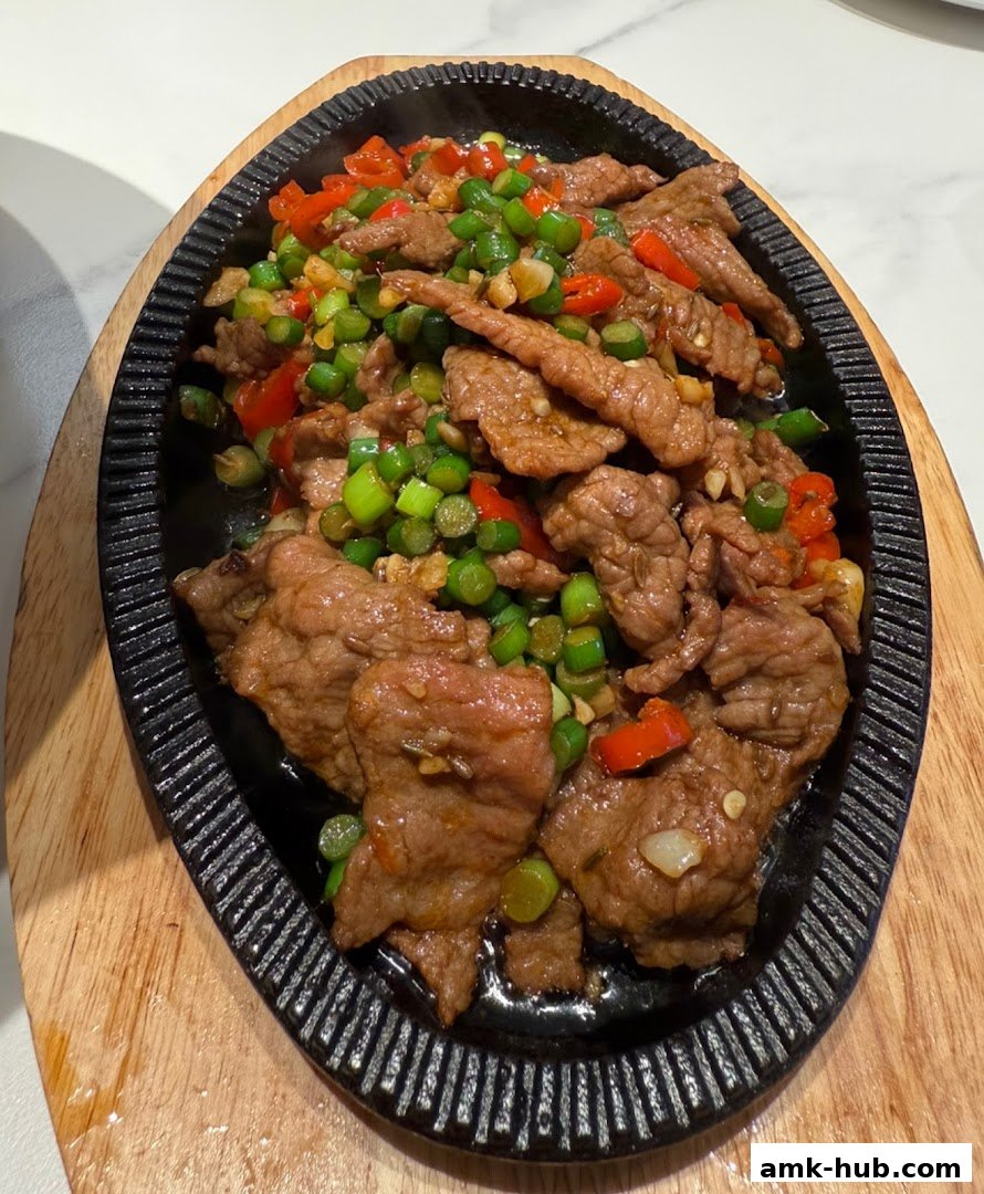 A sizzling plate of thinly sliced beef with chili peppers and green beans.