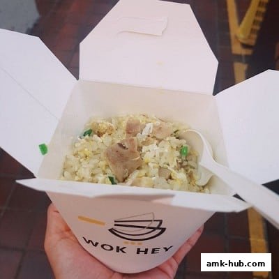 A hand holds a takeaway box filled with fried rice and meat.