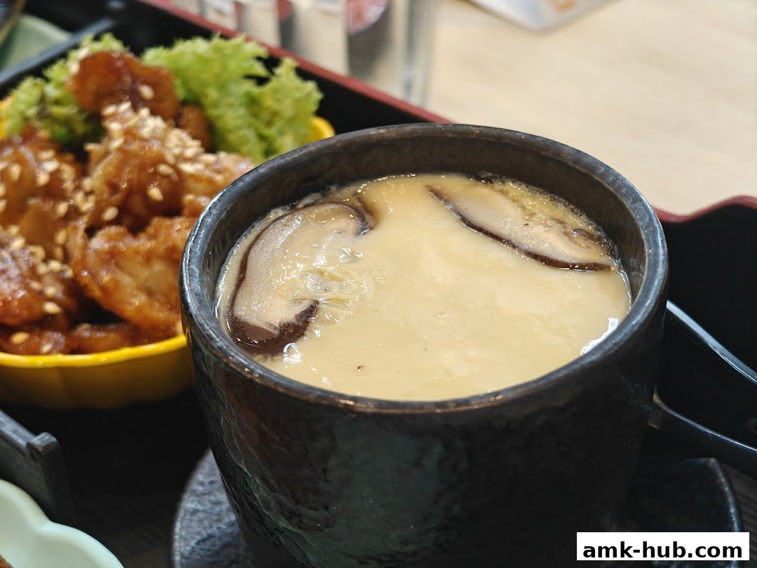 A close-up of a steaming cup of chawanmushi with shiitake mushrooms and a side of fried chicken.