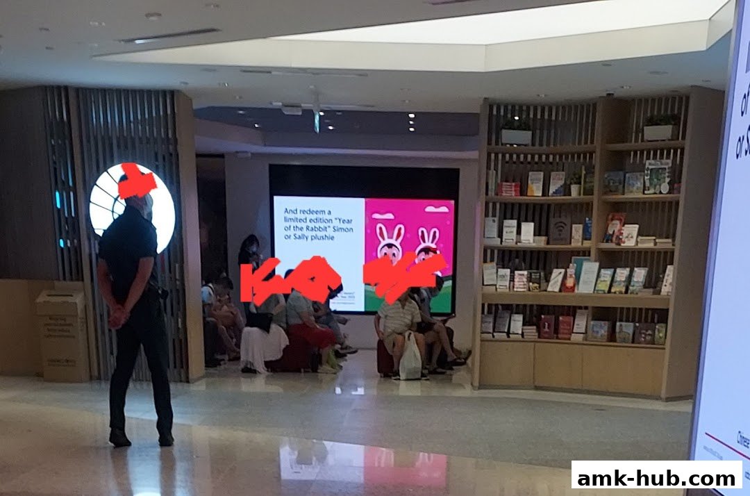 A bank branch interior with a promotional screen and bookshelves.