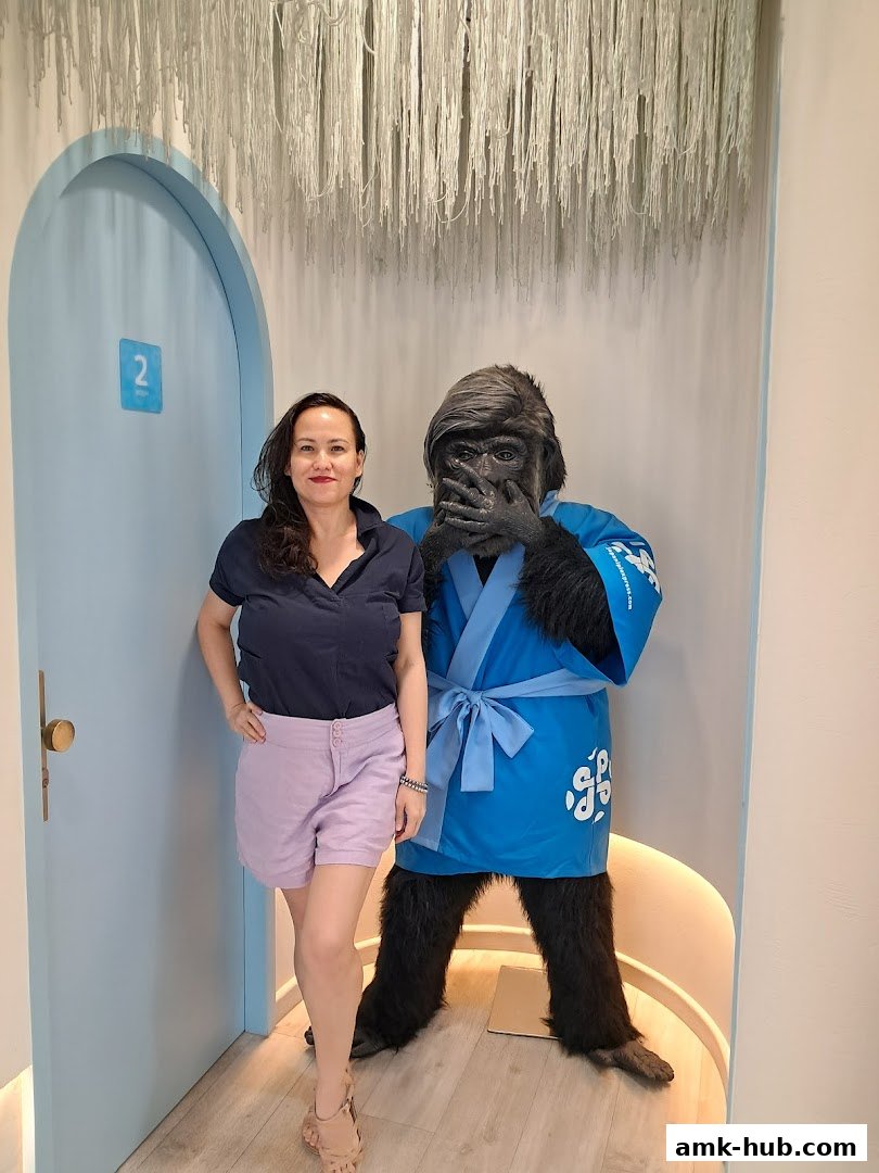 A woman poses with a gorilla mascot in a blue kimono inside a brightly lit shop.