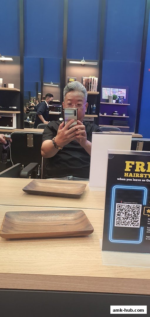 A man takes a selfie in a barber shop with mirrors reflecting the interior and staff.