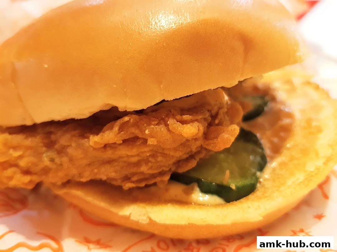 A close-up shot of a delicious Popeyes chicken sandwich with pickles and sauce.