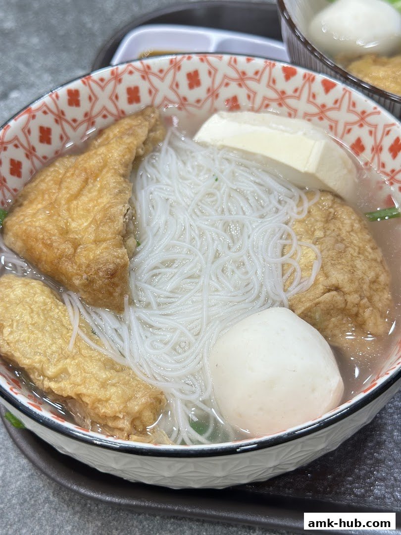 A close-up of a bowl of noodle soup with tofu, fish balls, and fried tofu.