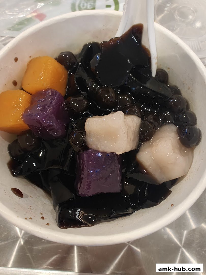 A bowl of grass jelly with taro balls, sweet potato balls, and pearls.