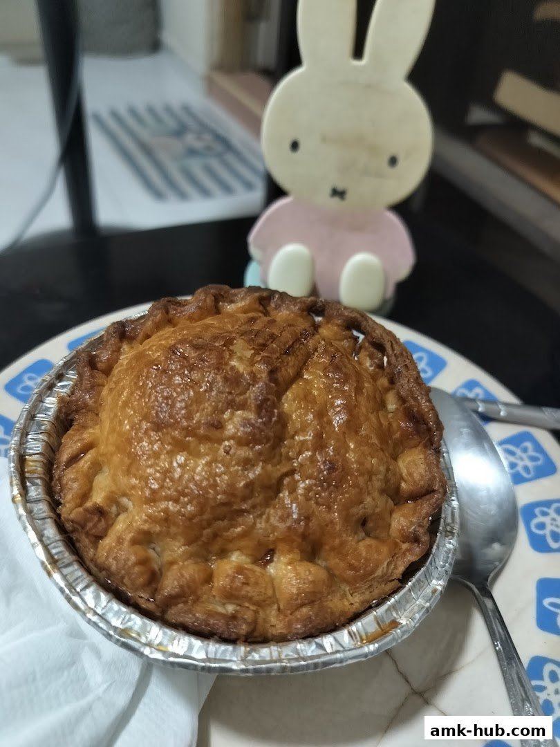 A golden-brown chicken pie in a foil container with a spoon and a Miffy figurine.