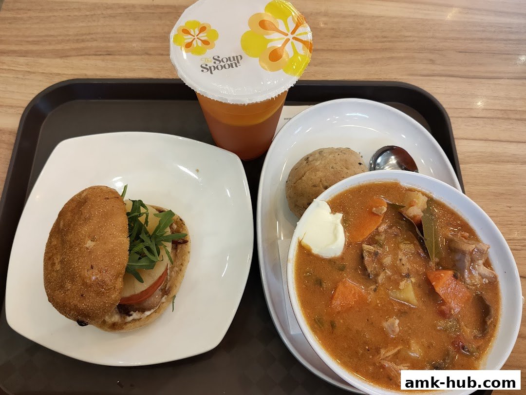 A hearty meal featuring a bowl of stew, a mini burger, a bread roll, and a drink.