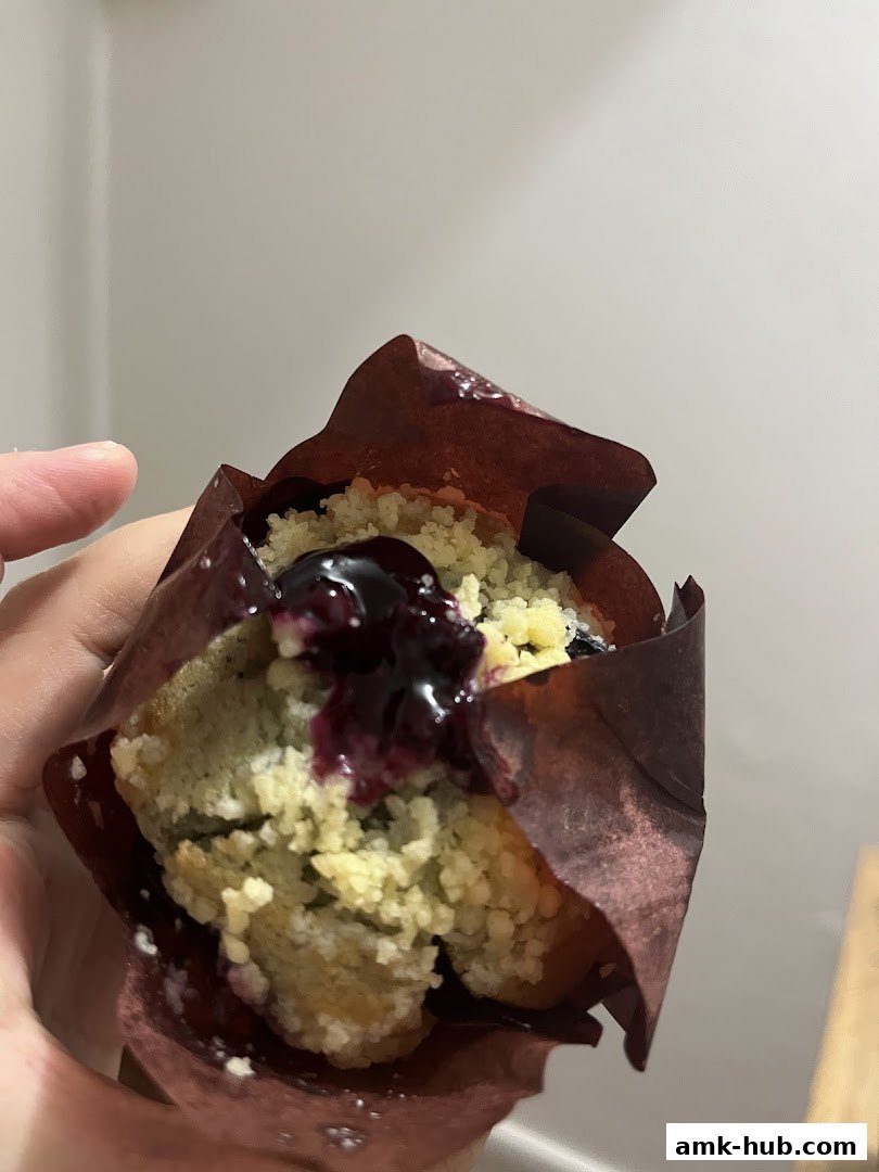 A hand holds a blueberry muffin with crumble topping and blueberry filling.