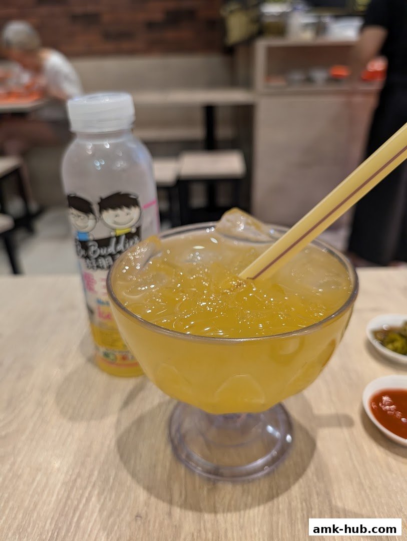 A refreshing yellow drink with ice and a straw, next to a bottle of 'Go Buddies' drink.