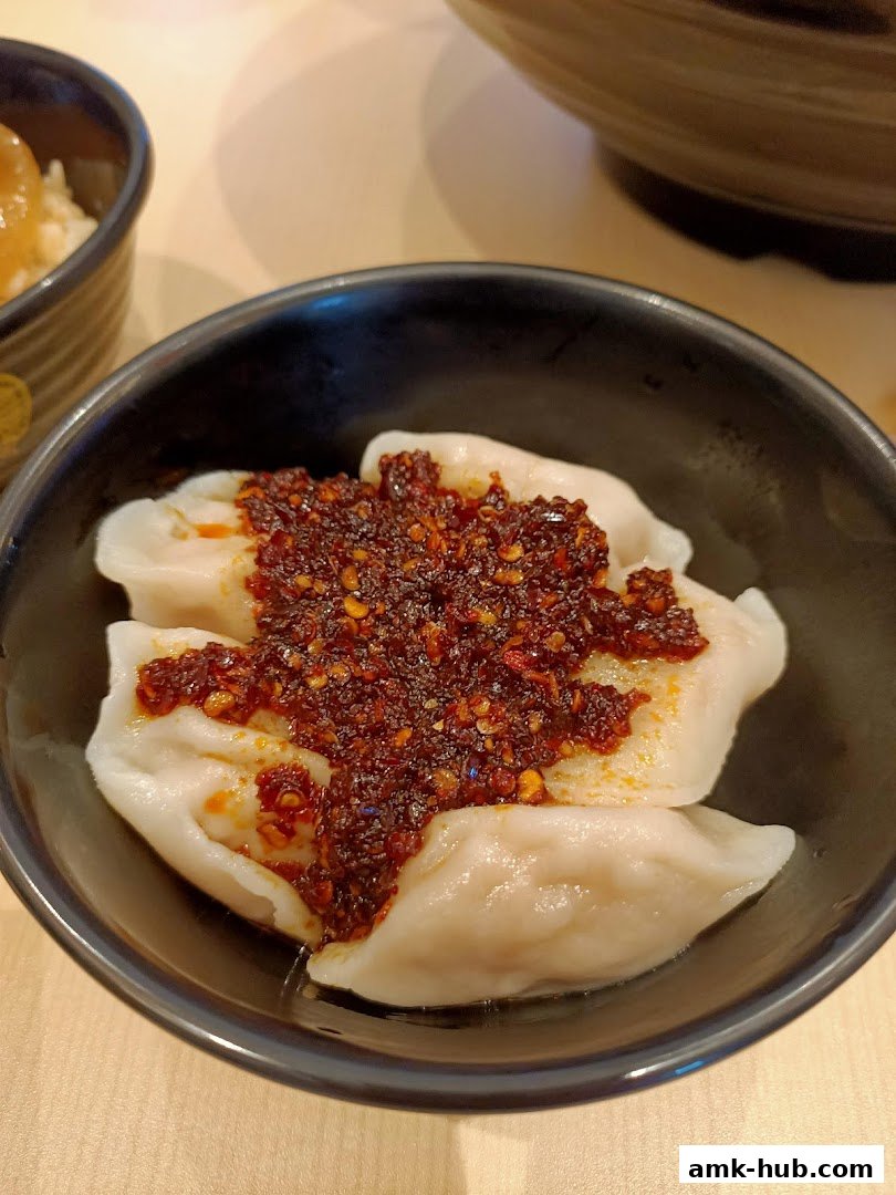 A close-up shot of dumplings topped with chili oil in a black bowl.