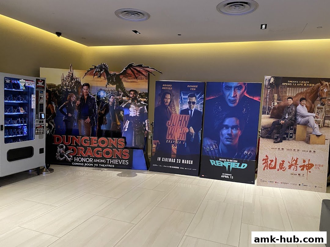 Movie posters and a vending machine displayed in a cinema lobby.