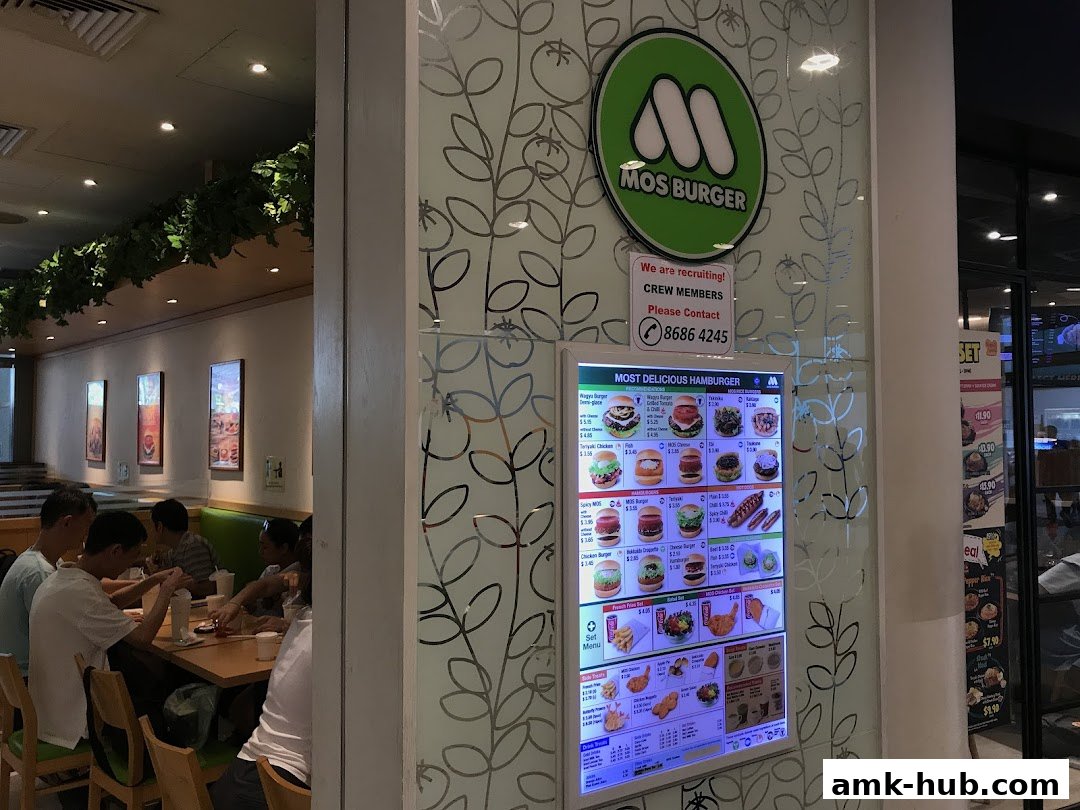 MOS Burger restaurant interior with a digital menu board and customers dining.