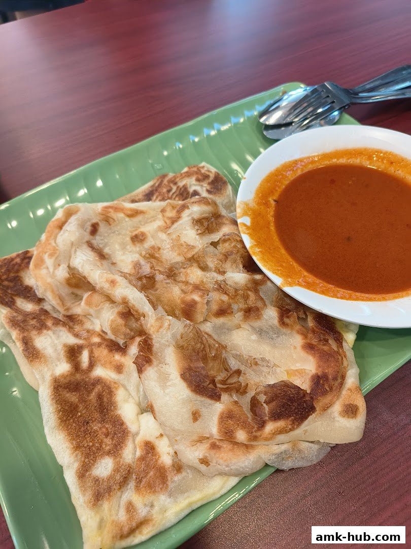 A close-up shot of flaky Roti Canai served with a side of curry sauce.