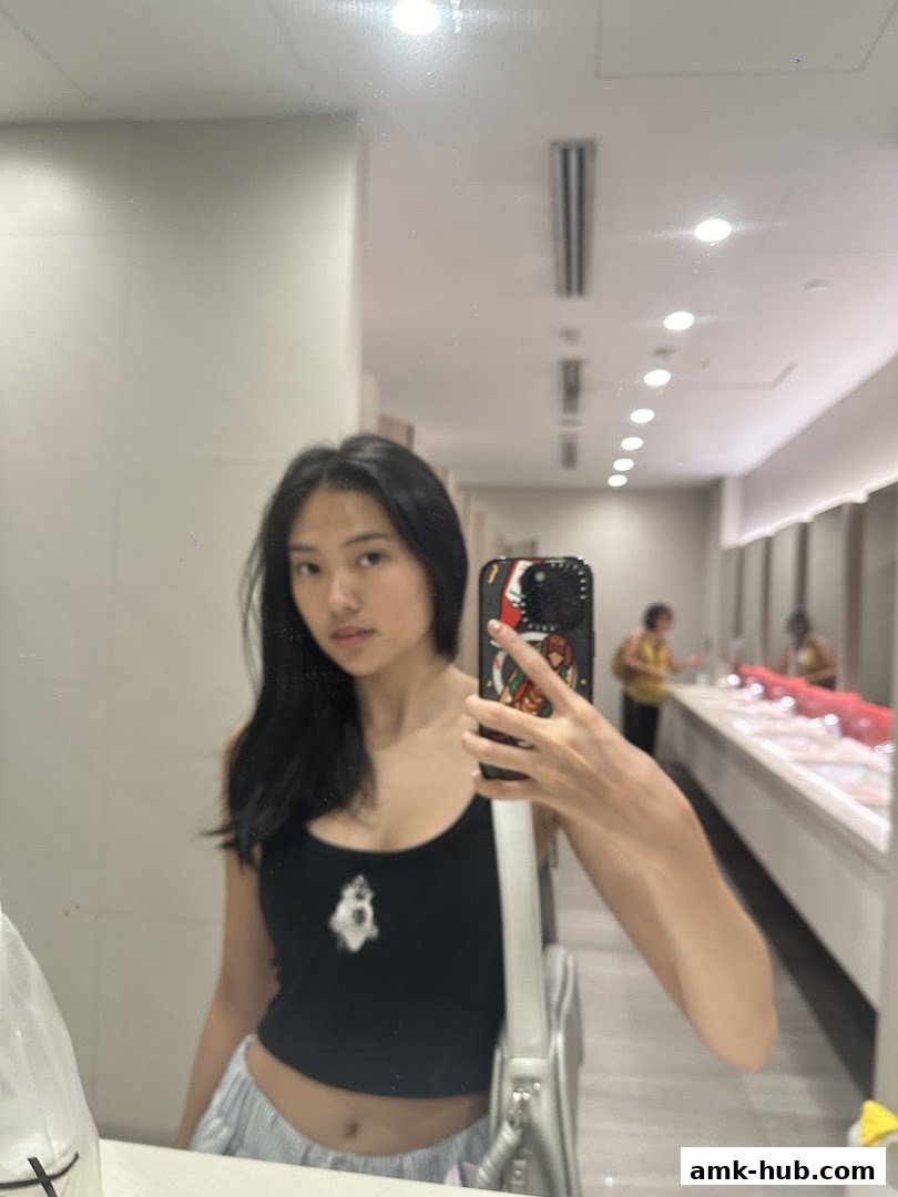 A young woman takes a mirror selfie in a brightly lit restroom.