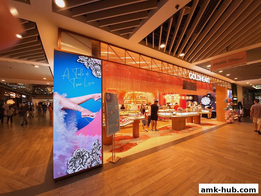 The Goldheart Jewelry store at AMK Hub features a bright, inviting interior with displays of jewelry and a large digital advertisement.