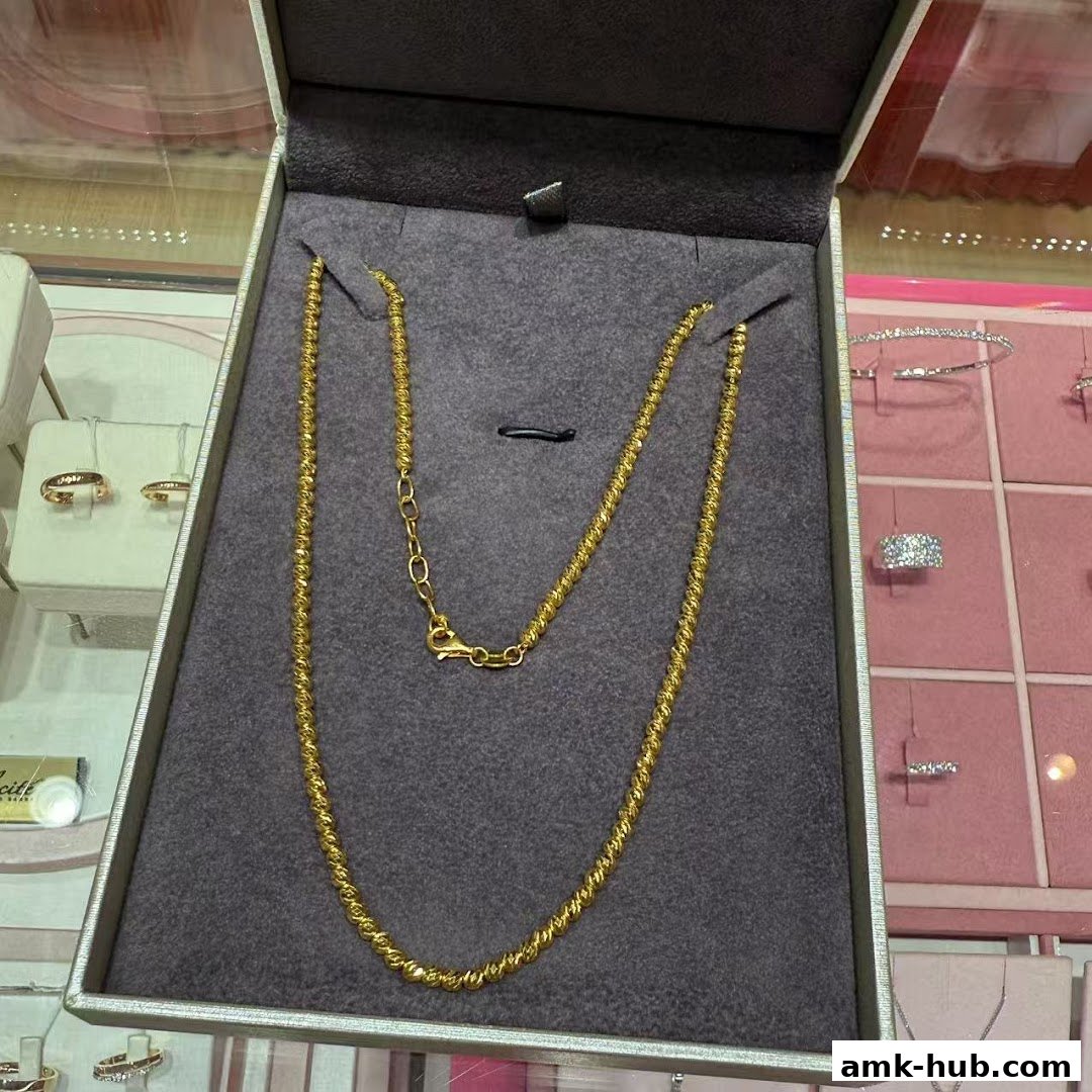 A gold necklace displayed in a jewelry box with other jewelry visible in the background.