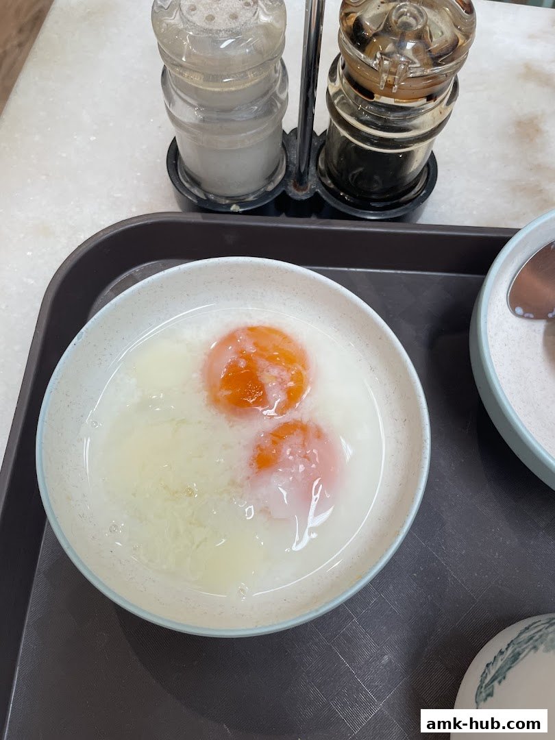 A close-up of two soft-boiled eggs in a bowl with seasoning shakers in the background.