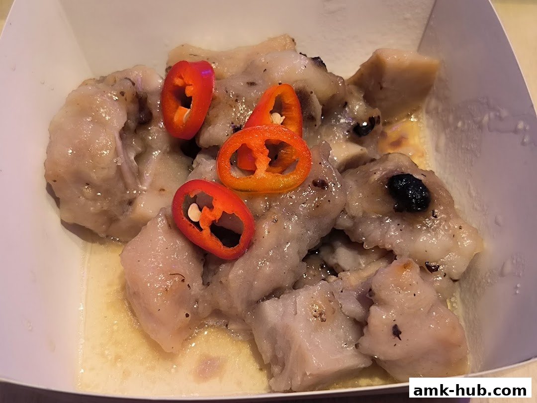 A close-up of dim sum dish with chili slices and dark beans in a white container.