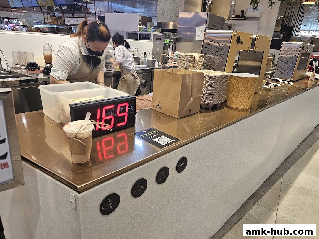 Staff preparing drinks behind a counter with a digital display and a drink.