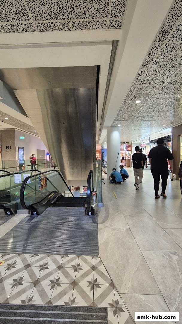 A mall interior with escalators, people walking, and cleaning staff.