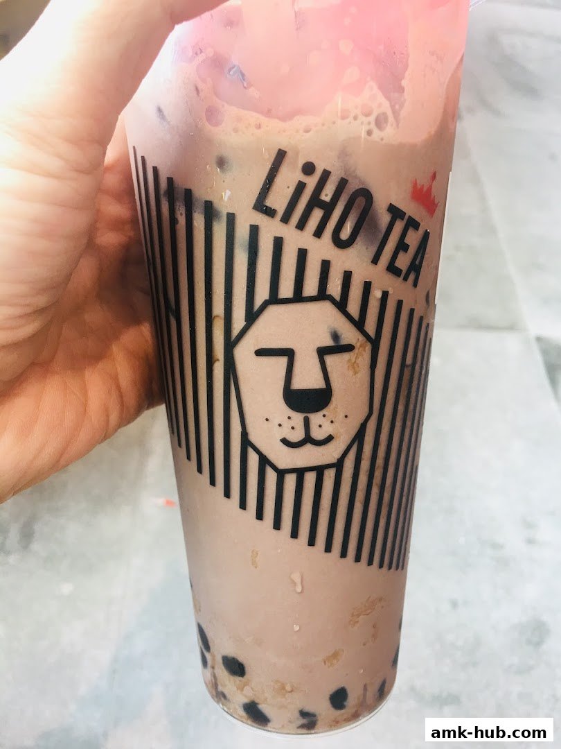 A hand holds a LiHO TEA cup filled with a brown beverage and tapioca pearls.