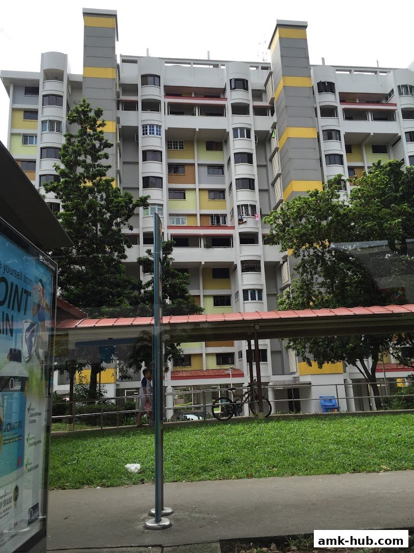 A colorful apartment building with a covered walkway and greenery in front.