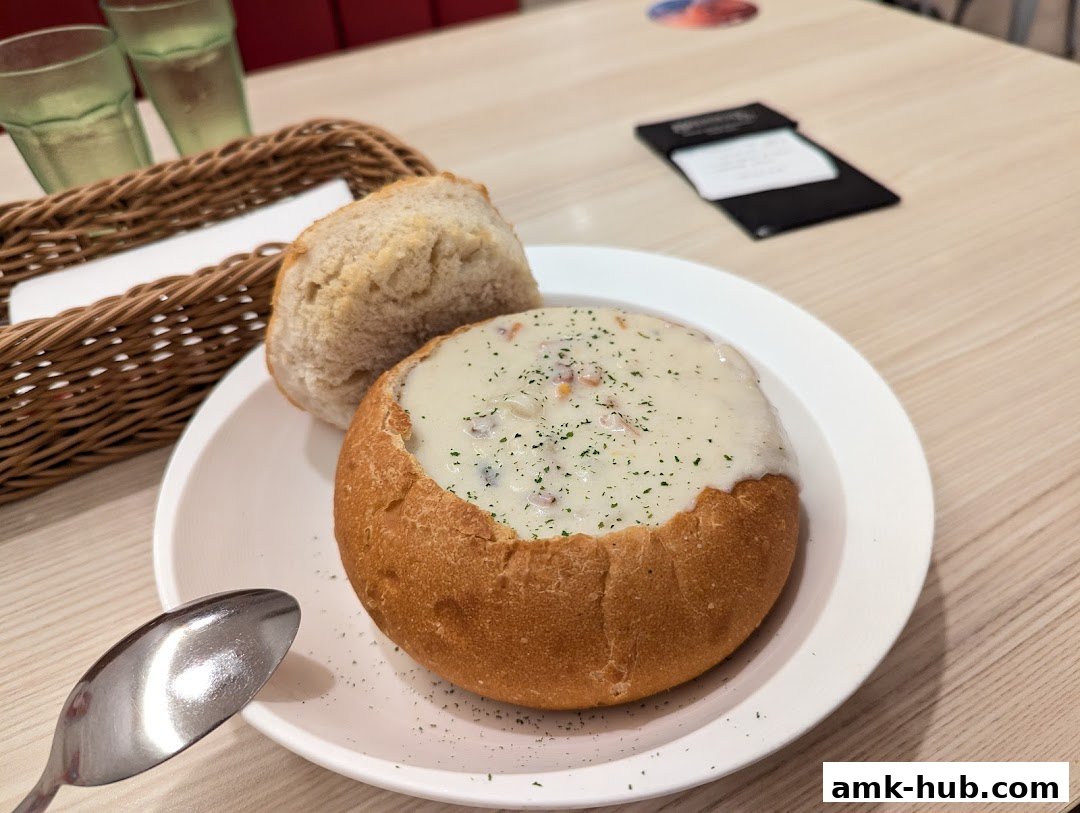 A bowl of creamy soup served in a bread bowl with a side of bread.
