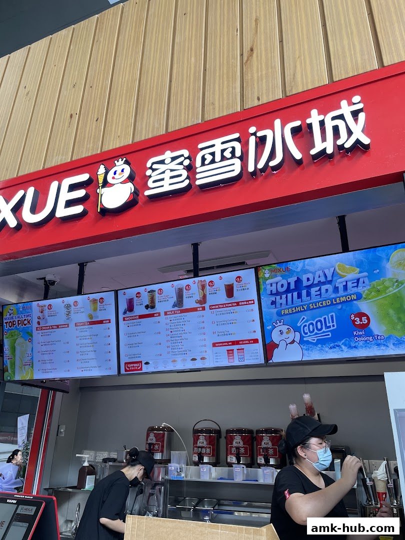A Mixue shop with digital menus displaying various drinks and a staff member preparing an order.
