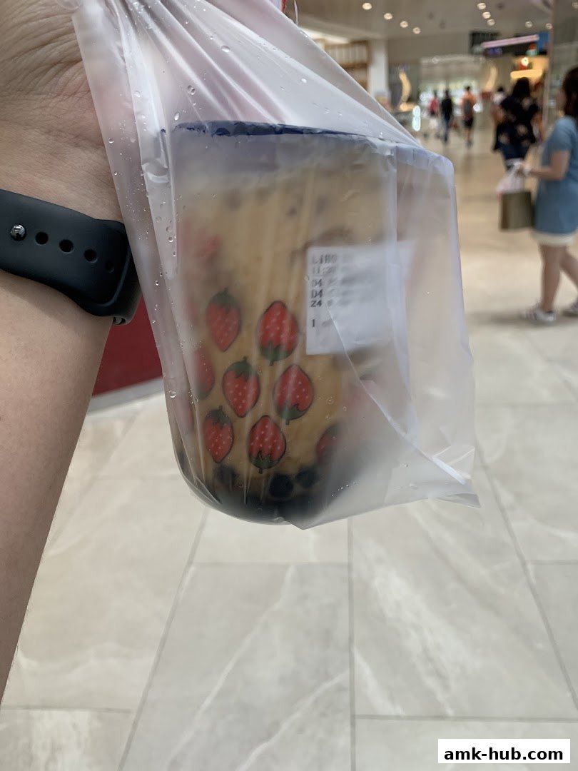 A hand holds a plastic bag containing a bubble tea with strawberry designs.