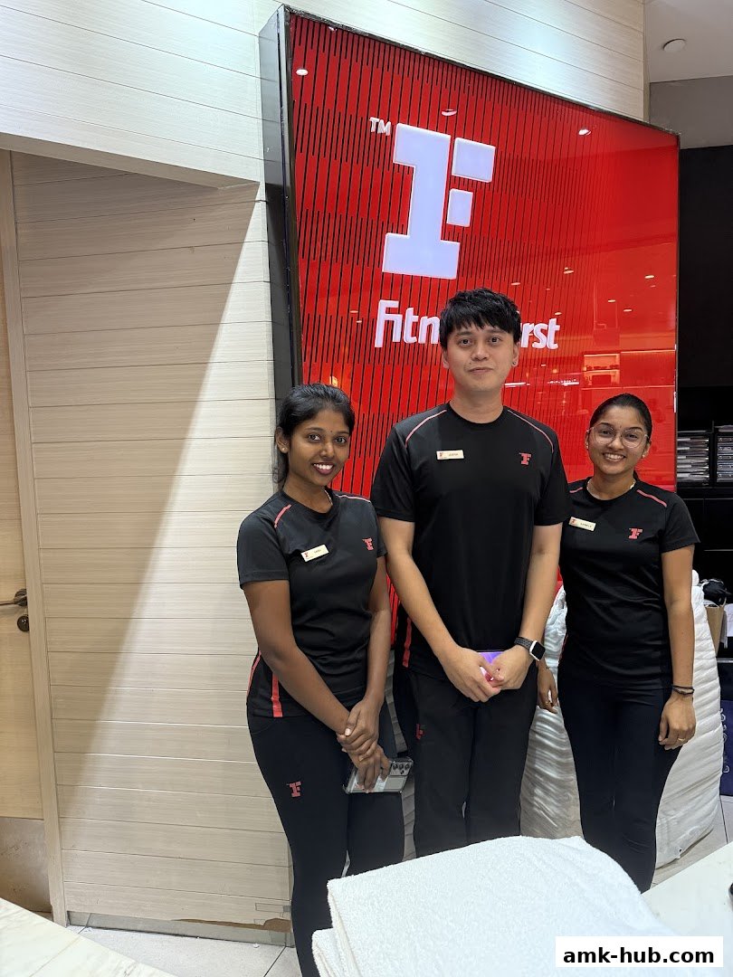 Three staff members stand in front of the Fitness First logo at AMK Hub.