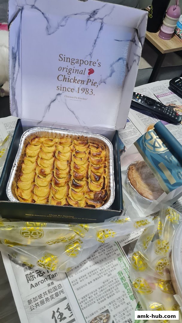 A large chicken pie in a baking tray, with a smaller pie and packaging in the background.