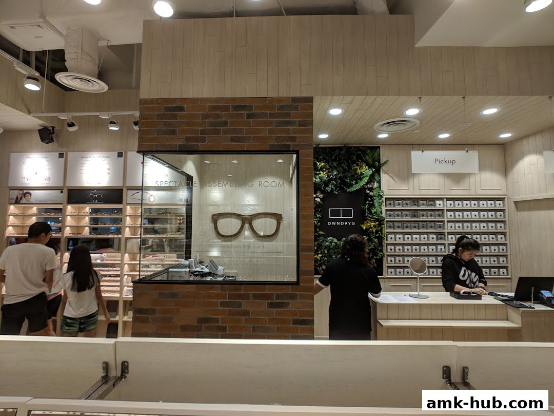 Interior view of an OWNDAYS optical shop with customers and staff at the counter.