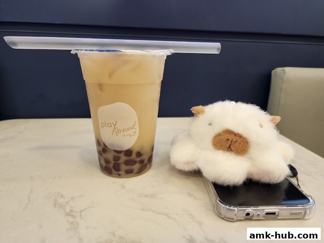 A bubble tea drink sits on a table next to a cute plush toy on a phone.