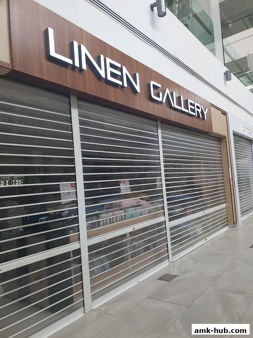 The storefront of Linen Gallery with its roller shutters down, displaying some products inside.