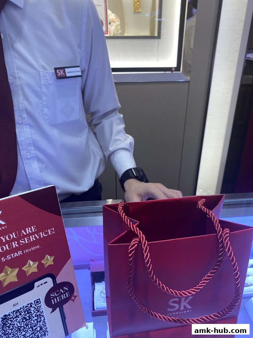 A staff member in a white shirt and tie stands behind a counter with a red shopping bag.