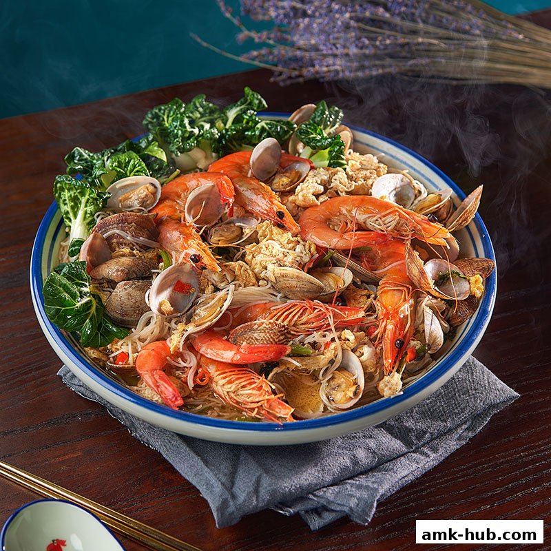 A steaming bowl of seafood noodles with prawns, clams, and greens, garnished with crispy bits.