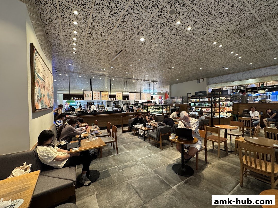 Interior of a busy Starbucks cafe with customers seated at tables and working on laptops.
