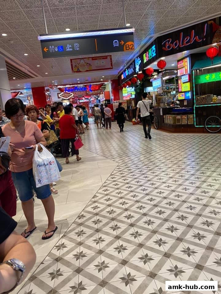 People queuing at a food stall with neon signs and red lanterns in a mall.