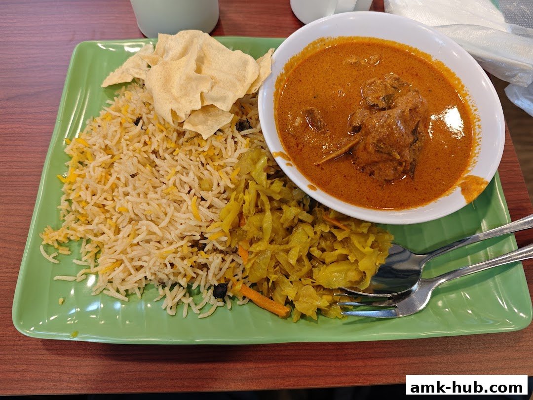 A plate of biryani rice with curry, pickled vegetables, and papadum.