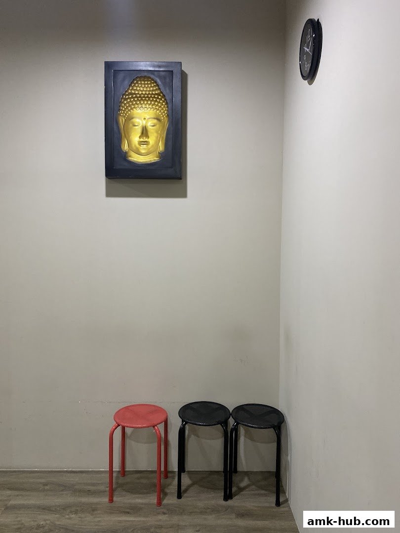 A golden Buddha head art piece hangs on a wall above three stools.