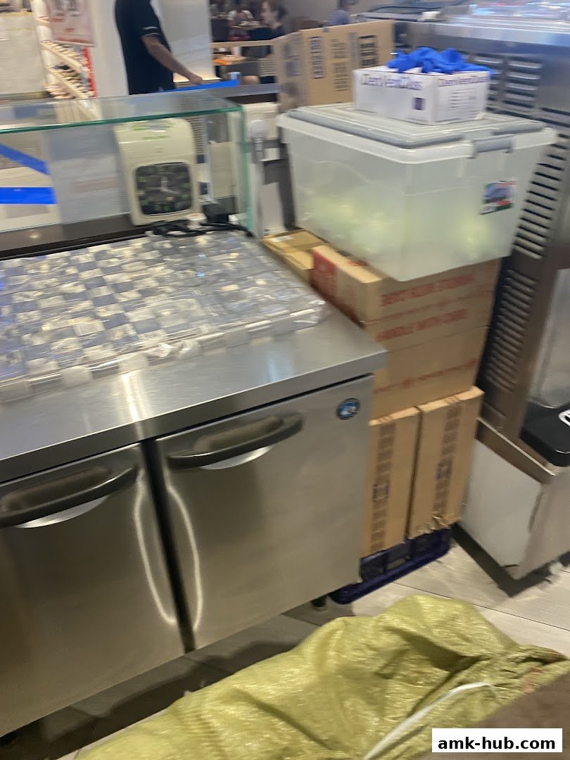 A stainless steel counter with a refrigerator and stacked boxes in a shop.