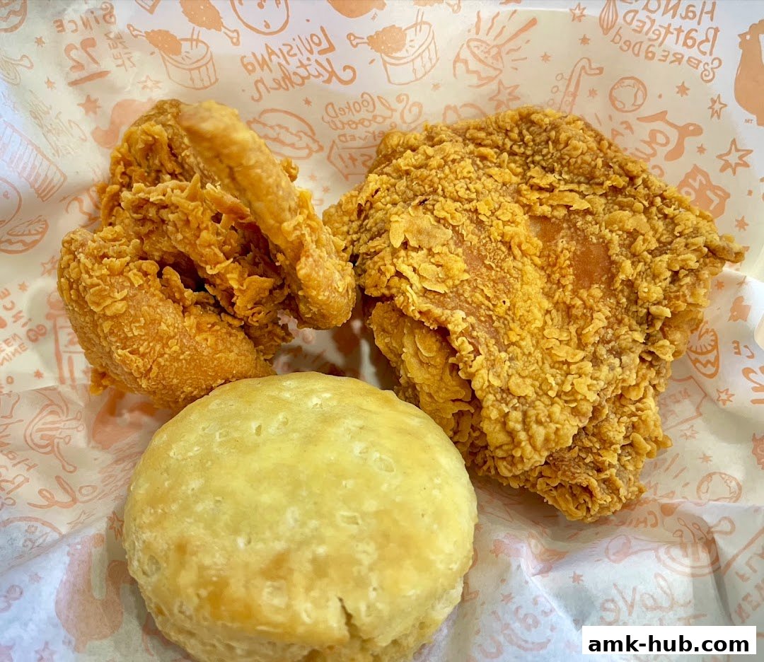 Crispy fried chicken pieces and a biscuit served on branded paper.