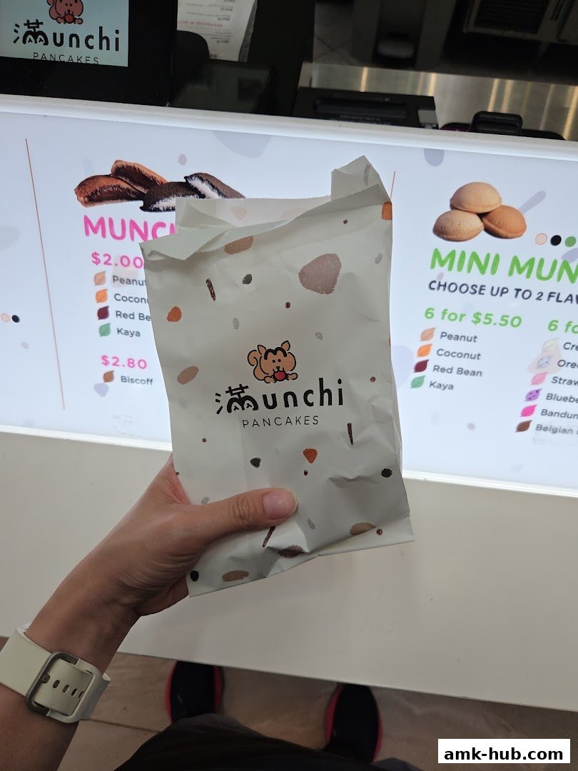 A person holds a paper bag in front of a digital menu displaying pancake options and prices.