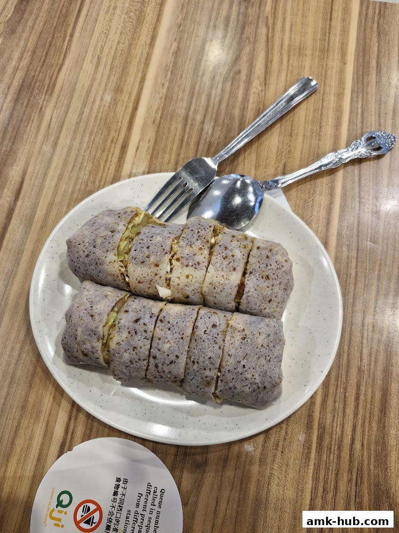 Two freshly prepared spring rolls are served on a white plate with a fork and spoon.