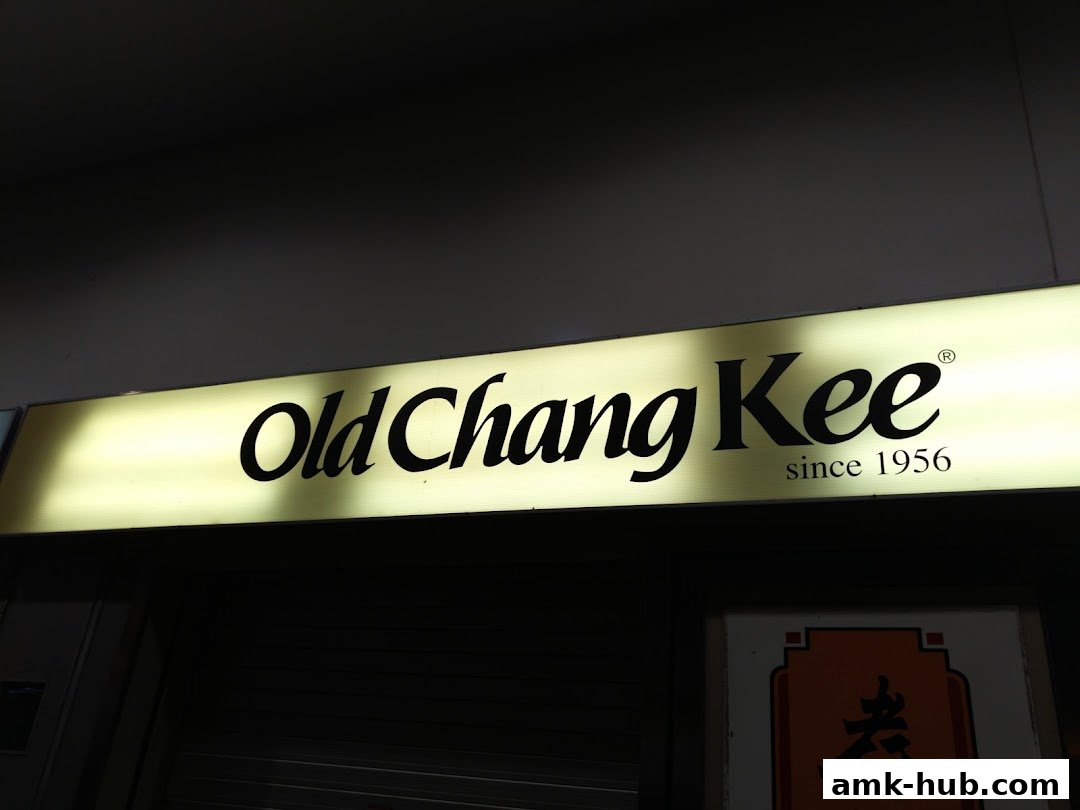 A lit sign for Old Chang Kee, established in 1956, above a dark storefront.