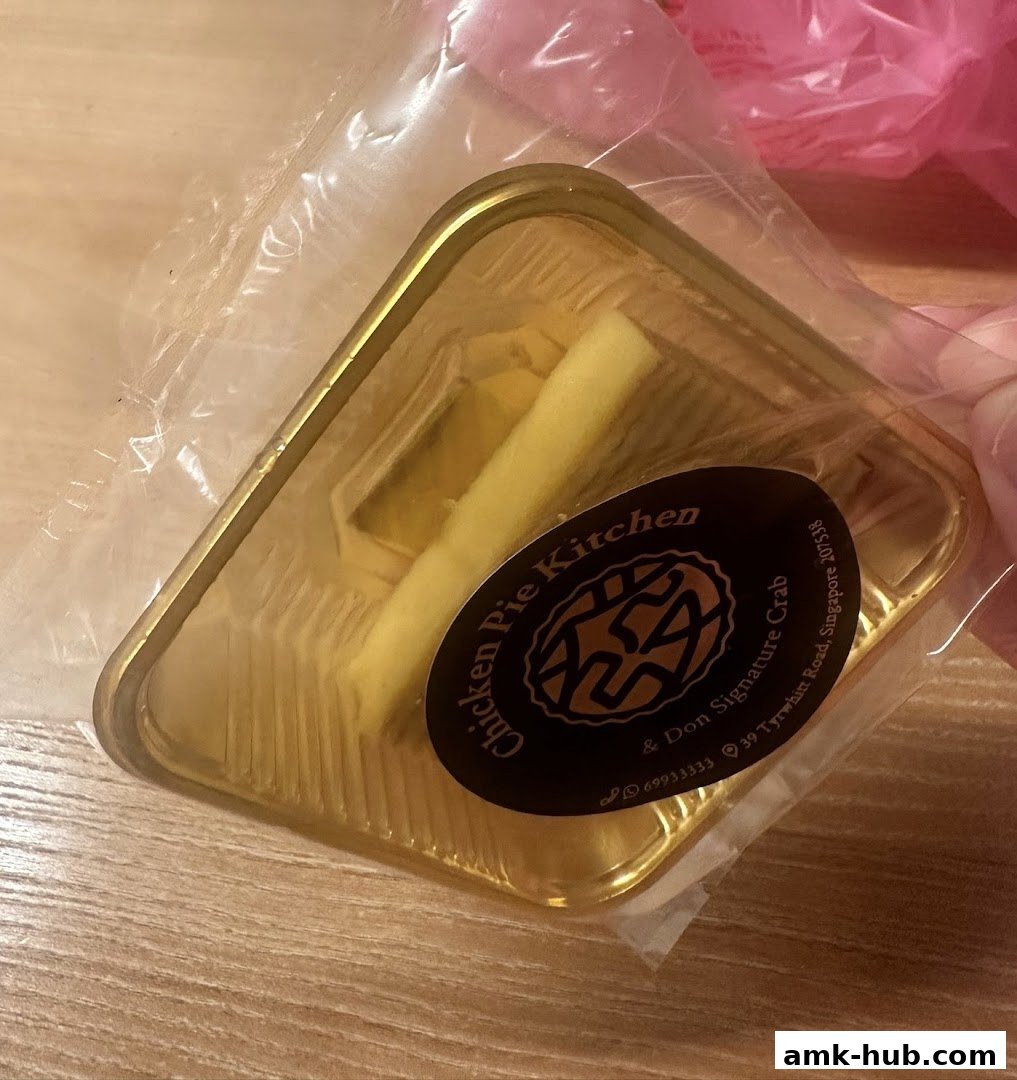 A person holds a golden takeout container with a piece of food inside, branded with Chicken Pie Kitchen.
